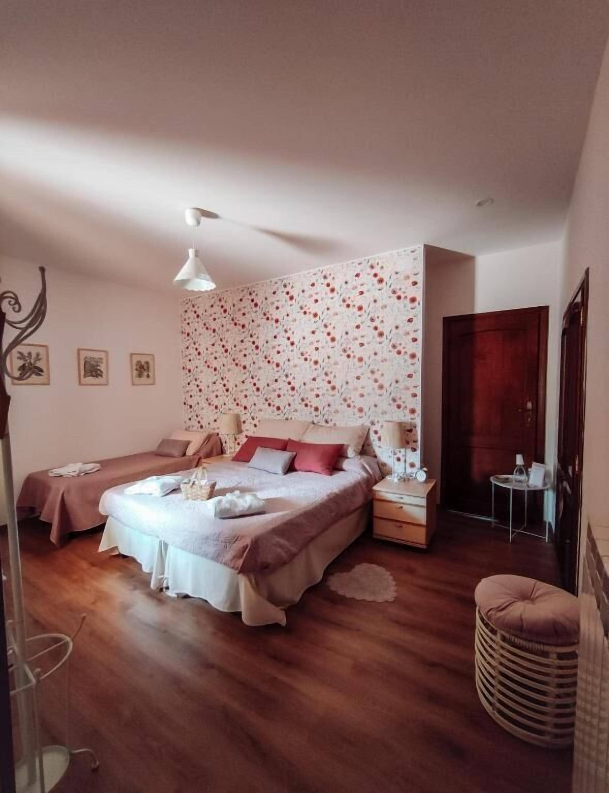 Een slaapkamer met een groot bed, twee nachtkastjes, een klein tafeltje, een stoel, een lamp en een wand met een bloemenmotief.
