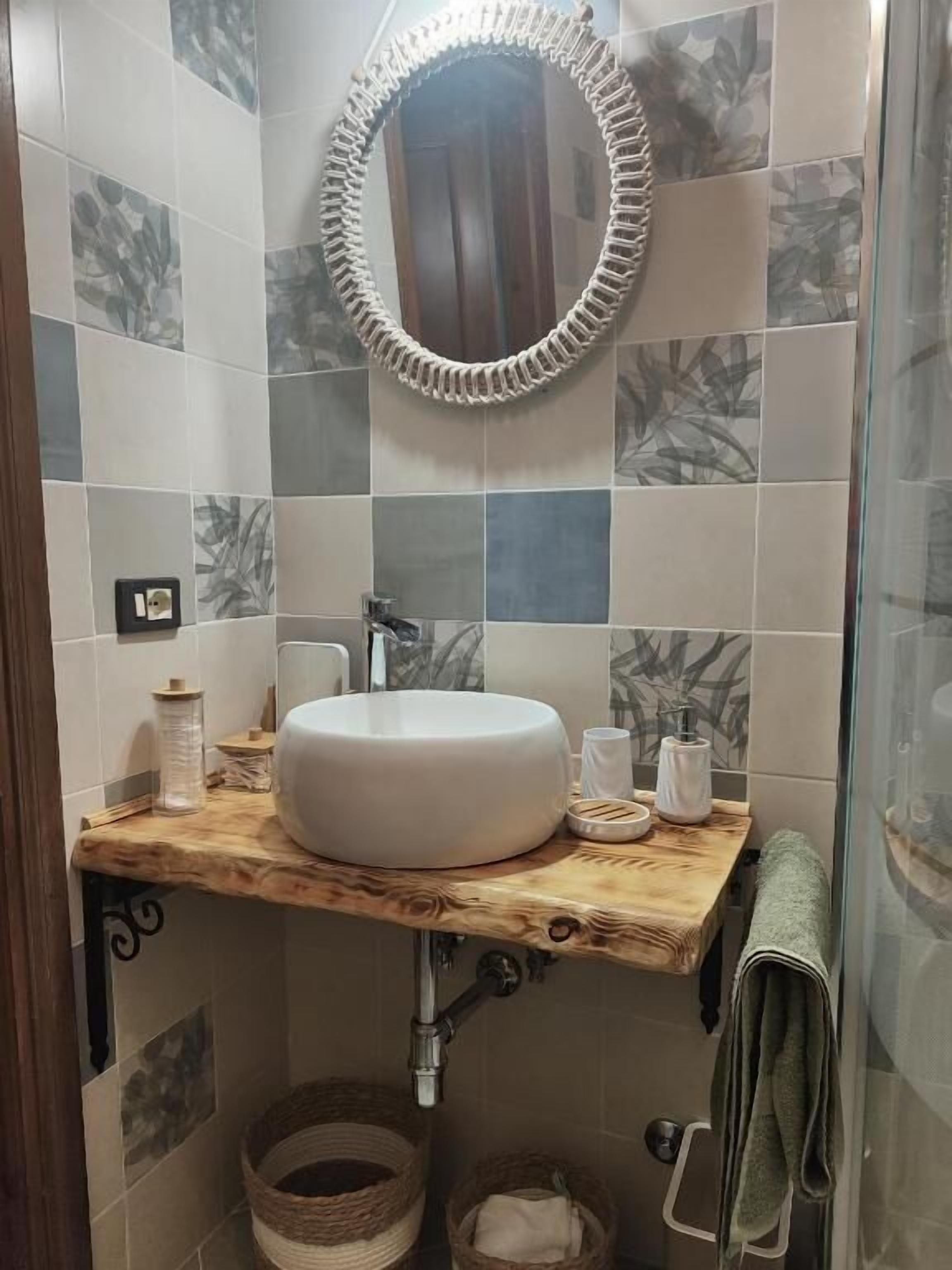 Un bagno con uno specchio rotondo, un mobile bagno in legno, un lavandino bianco e un porta asciugamani.