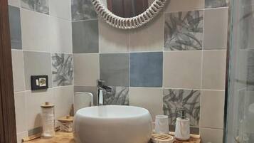 Un bagno con uno specchio rotondo, un mobile bagno in legno, un lavandino bianco e un porta asciugamani.