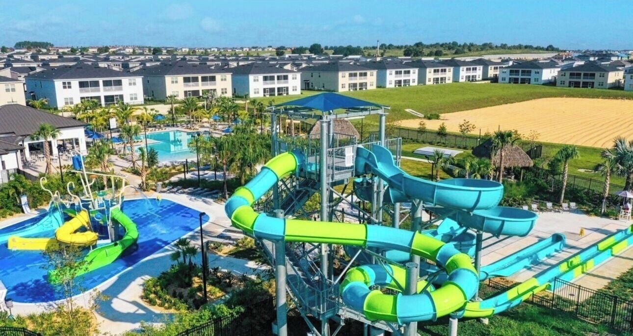 A water park with multiple slides and a pool area, surrounded by buildings and a beach.