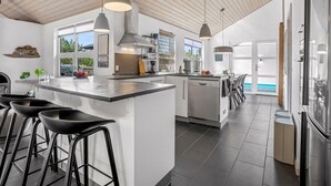 Una cocina moderna con una isla central, taburetes de bar, iluminación colgante y vistas al exterior.