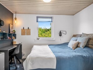 Ein Schlafzimmer mit einem Bett, einem Schreibtisch, einem Stuhl, einem Fenster mit Blick auf Grünflächen und einer Wandlampe.