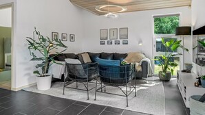 Una sala de estar moderna con un sofá, dos sillones, una mesa de centro y un amplio ventanal con vistas a la vegetación.