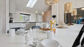 Un'elegante zona pranzo con un tavolo bianco apparecchiato per due, una cucina sullo sfondo e un lucernario.
