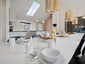 A modern dining area with a white table set for two, a kitchen in the background, and a skylight above. - 5 Star Holiday Home in Romo (Rømø)