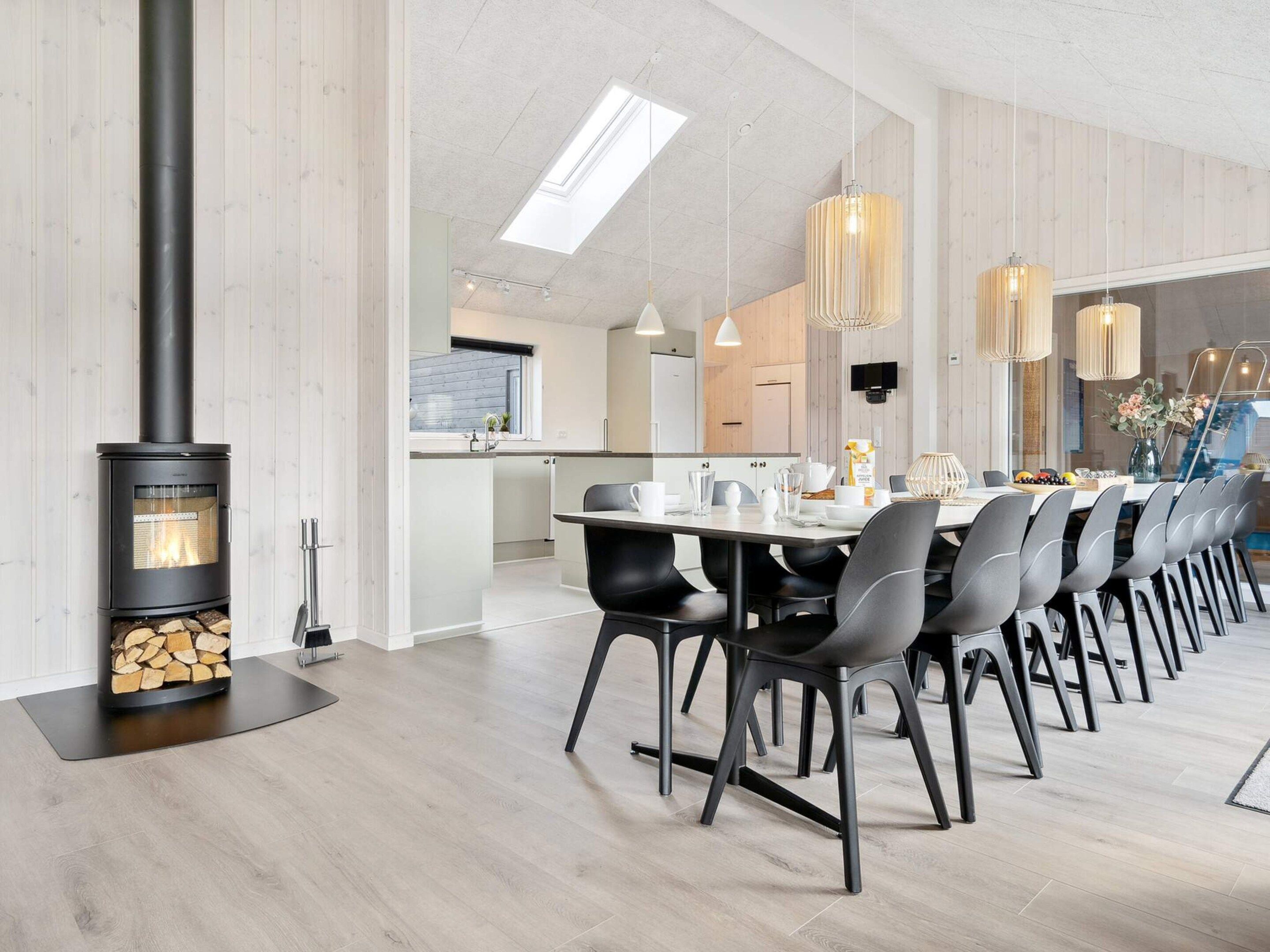 Una cocina moderna con estufa de leña, un comedor con una mesa larga y sillas, y una isla de cocina con pileta y encimera.