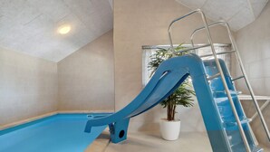 Una piscina interna con uno scivolo blu e una scala in metallo.