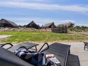 A view of a modern building complex with multiple structures, a grassy area, and lounge chairs with a blanket and book. - 5 Star Holiday Home in Romo (Rømø)