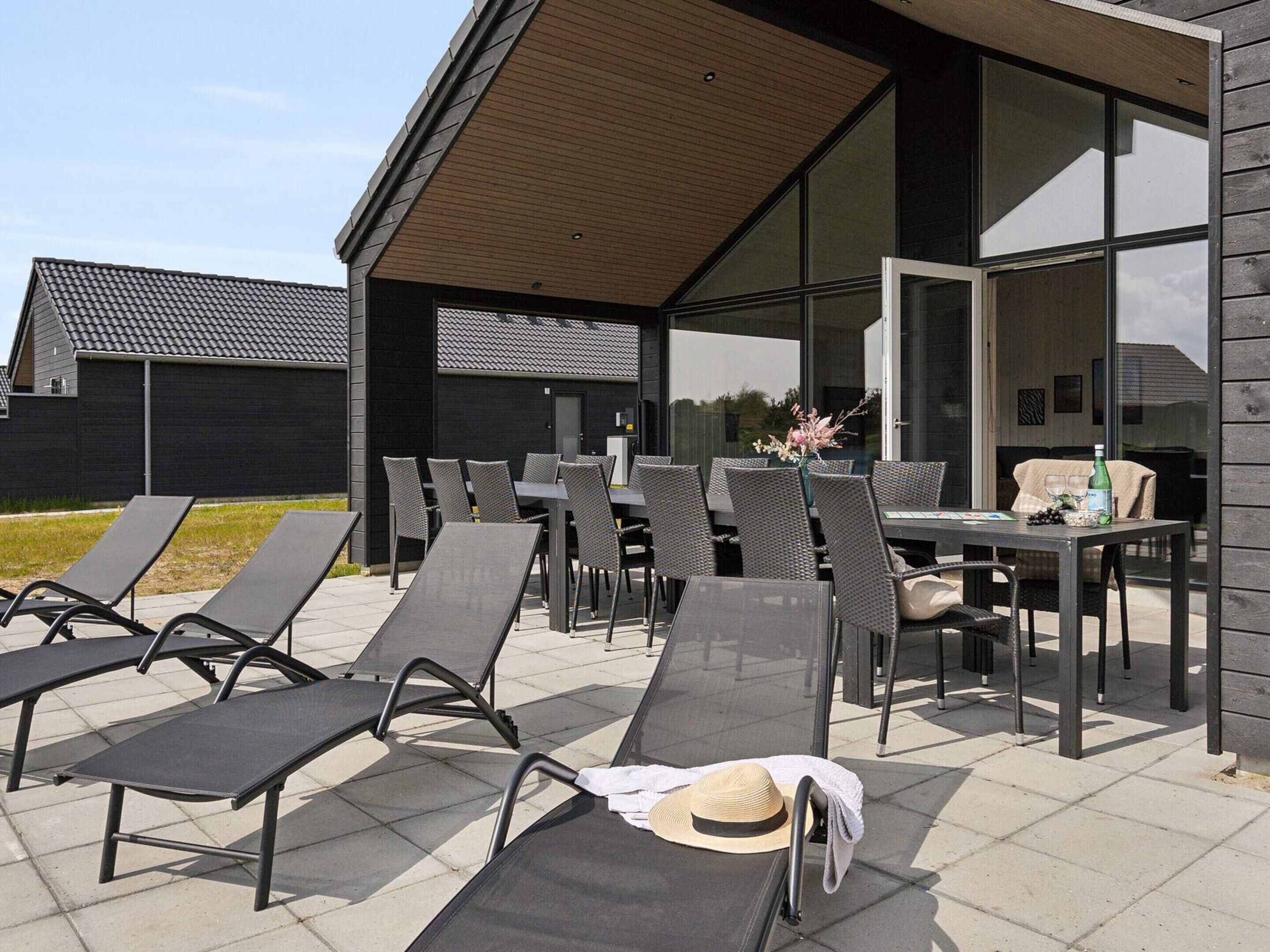 An outdoor seating area with sun loungers and tables, a modern building with large windows, and a wooden sloped roof.