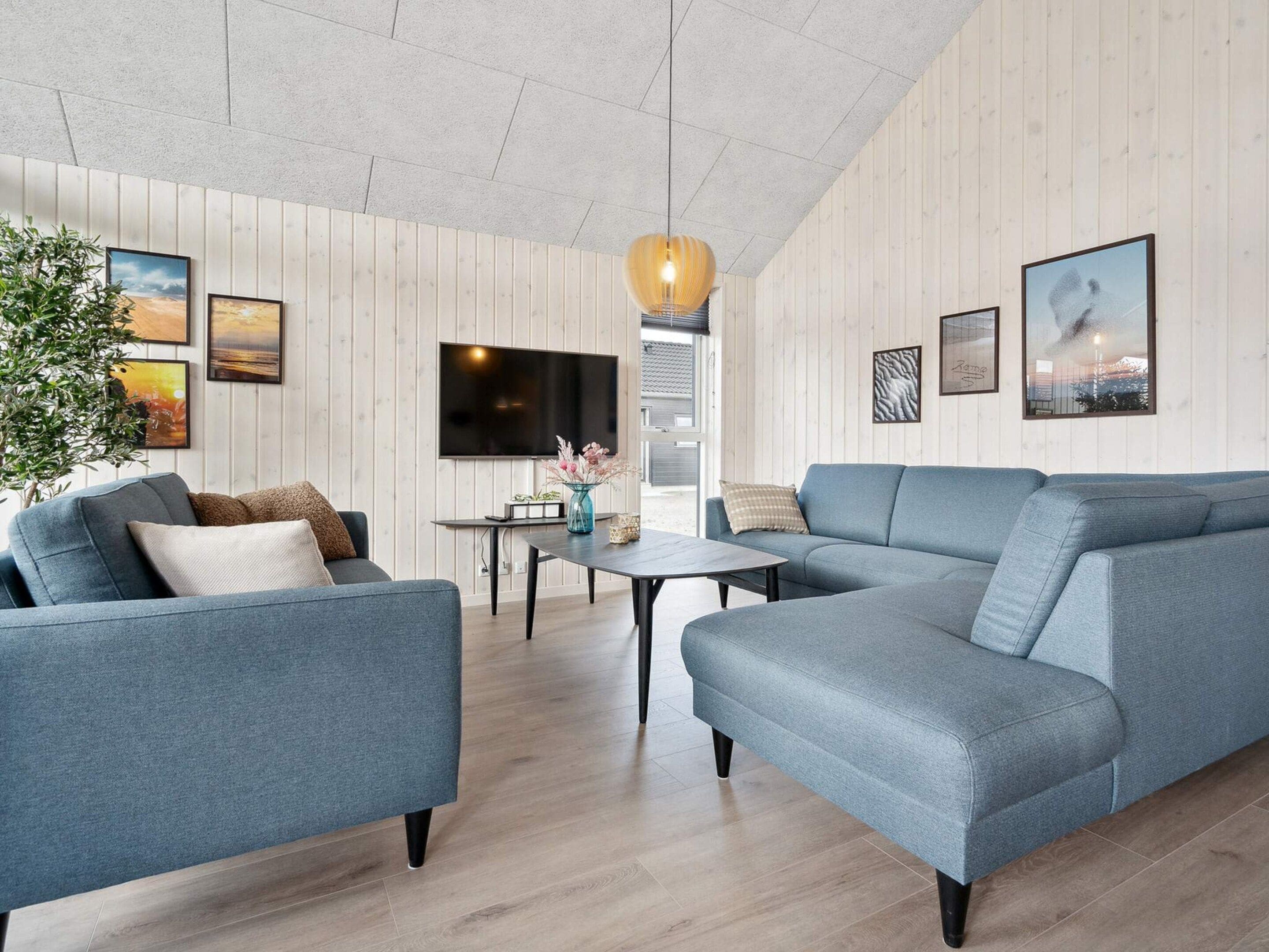 Una sala de estar moderna con un sofá gris, un televisor de pantalla plana montado en la pared y piso de madera.
