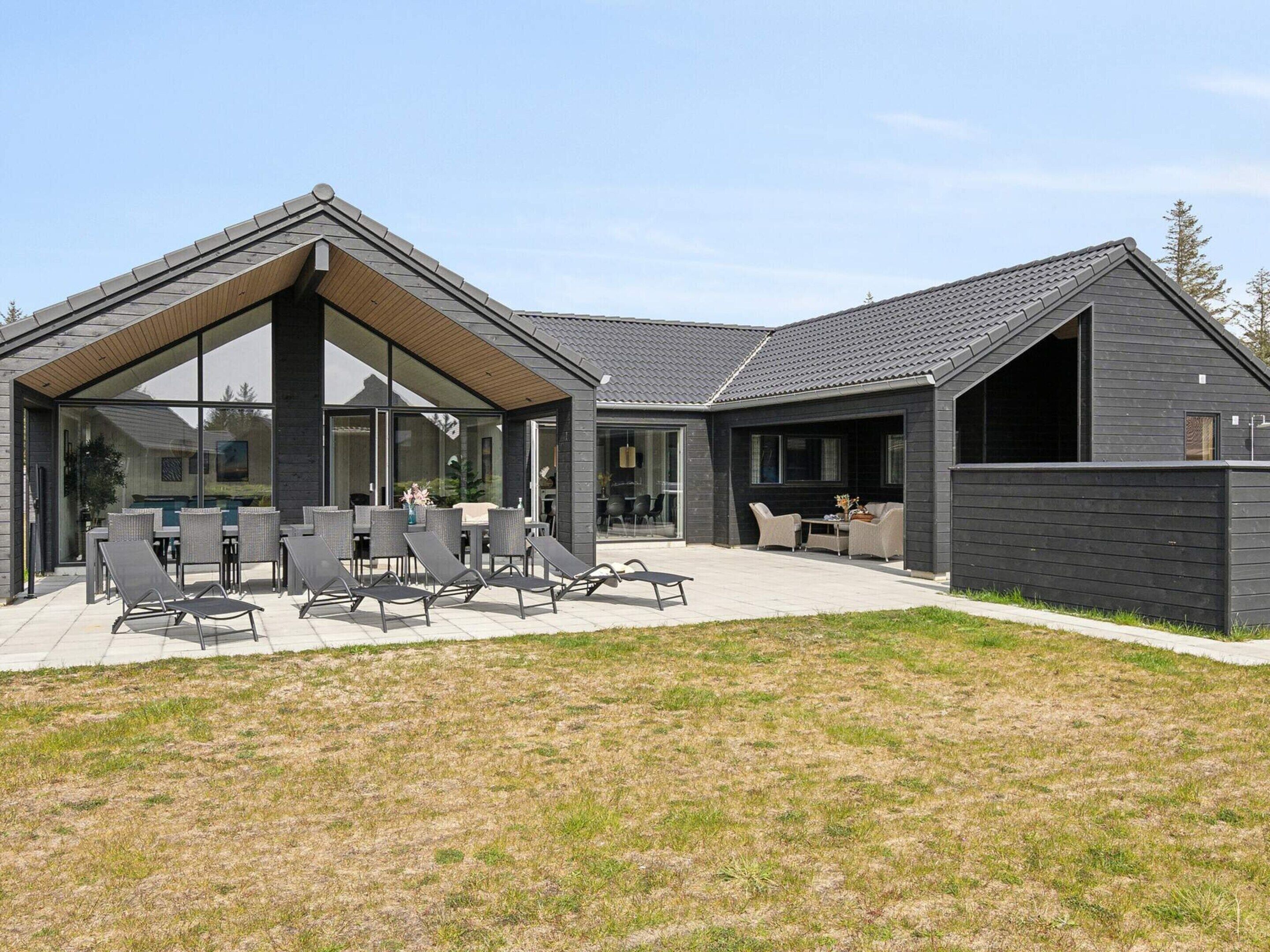 A modern house with a covered patio, outdoor seating, and a large glass window.