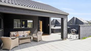 A covered outdoor seating area with wicker furniture and a barbecue grill.