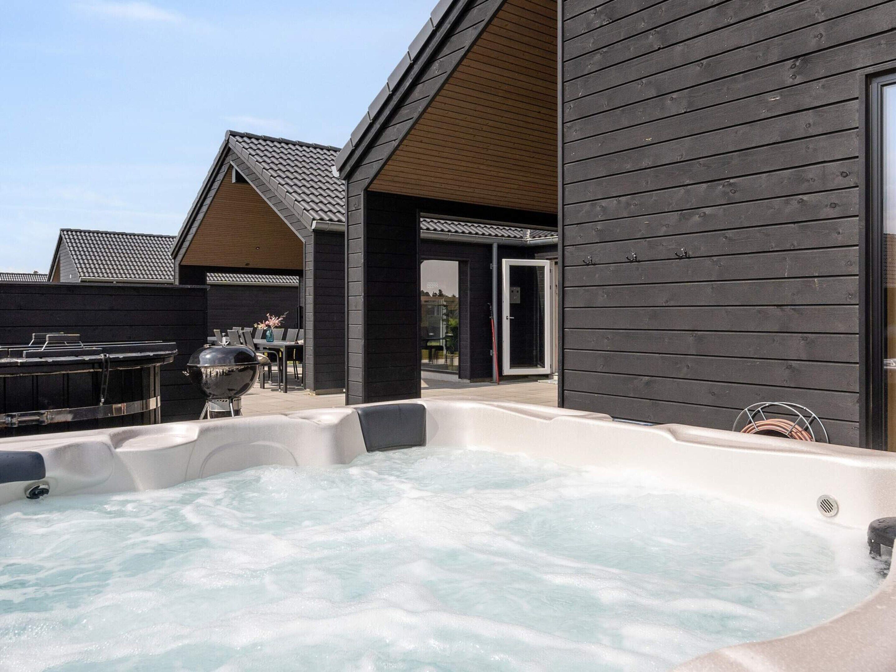 A hot tub area with a wooden deck, a barbecue grill, and a covered seating area.