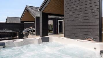 A hot tub area with a wooden deck, a barbecue grill, and a covered seating area.