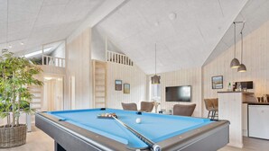 Un tavolo da biliardo in una stanza con soffitto alto, pareti in legno e angolo cottura.