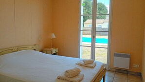 Ein Schlafzimmer mit Bett, Nachttisch, Lampe, einer Schiebeglastür zum Pool und einem Wandheizkörper.