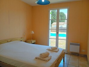 Ein Schlafzimmer mit Bett, Nachttisch, Lampe, einer Schiebeglastür zum Pool und einem Wandheizkörper.