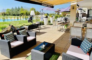 Eine Terrasse im Freien mit Korbmöbeln, im Hintergrund ein Pool und ein Schild mit der Aufschrift 'VENDÉE SERIE'.