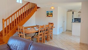 Ein Essbereich mit Holztisch und -stühlen, eine Treppe, ein Küchenbereich und ein Wohnzimmer mit Ledersofa.