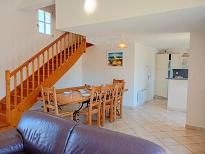 Ein Essbereich mit Holztisch und -stühlen, eine Treppe, ein Küchenbereich und ein Wohnzimmer mit Ledersofa.