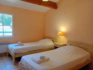 Een kamer met twee eenpersoonsbedden, een raam, een nachtkastje met een lamp en een radiator.
