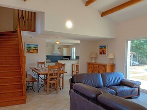 Ein geräumiger Wohnbereich mit einer Couch, einem Esstisch, Stühlen und einer Küche im Hintergrund.