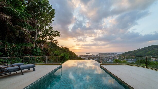 Ein Infinity-Pool auf dem Dach mit Blick auf eine Stadtlandschaft und Hügel.