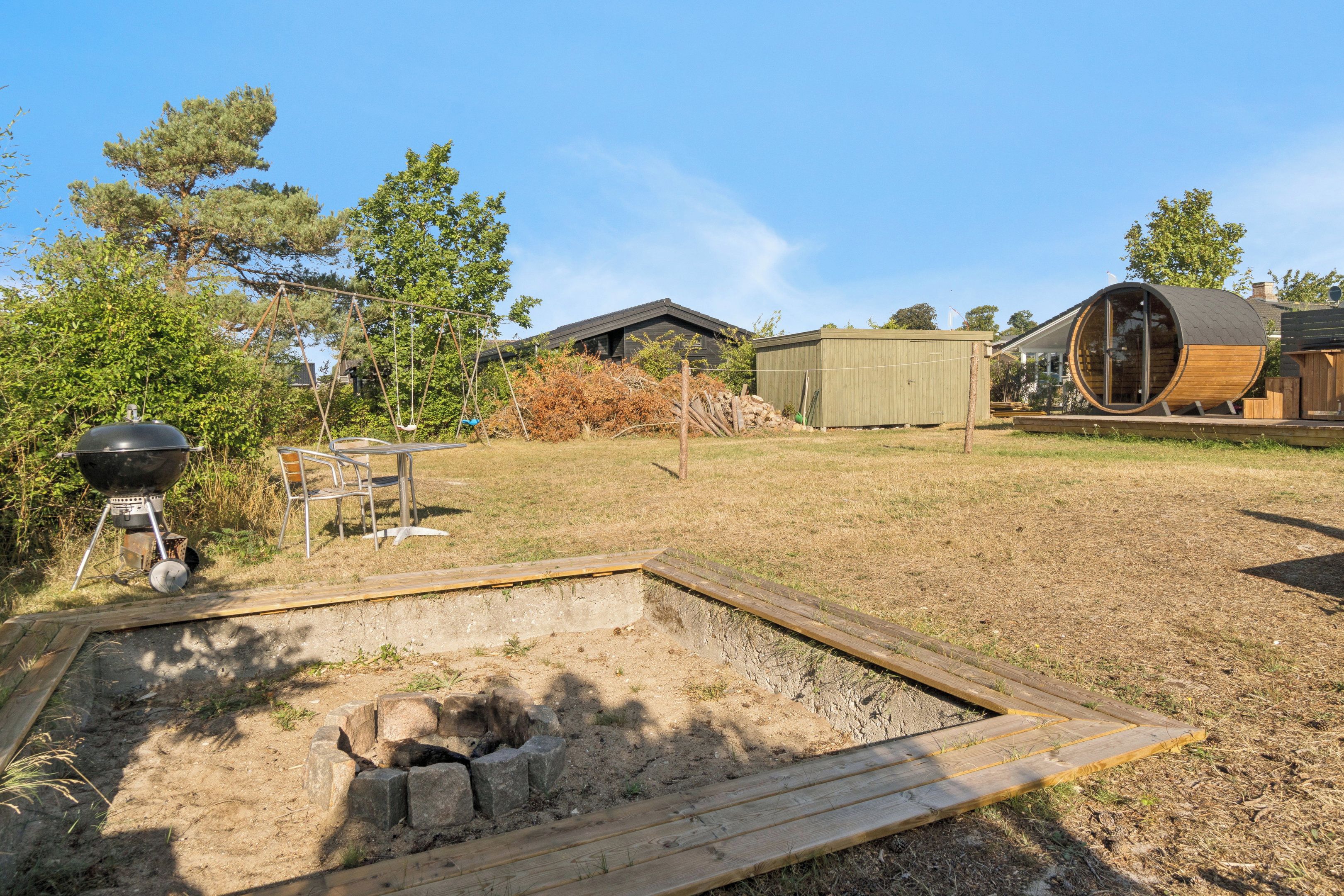 A backyard with a barbecue grill, a swing set, a wooden deck, and a circular wooden structure.