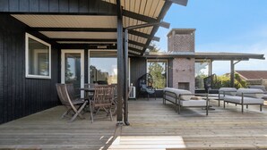 Una terraza de madera con mobiliario exterior, incluyendo sillas y sofás, y una chimenea de ladrillo.