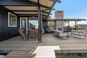A wooden deck with outdoor furniture, including chairs and sofas, and a brick fireplace. - Holiday idyll with water views (Rønde)