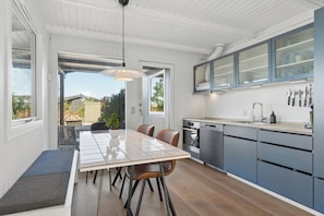 A modern kitchen with a dining area, featuring a large window, built-in cabinets, and a variety of kitchen appliances. - Holiday idyll with water views (Rønde)