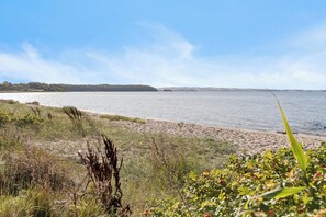 A beach with a clear sky, calm water, and a distant landmass. - Holiday idyll with water views (Rønde)