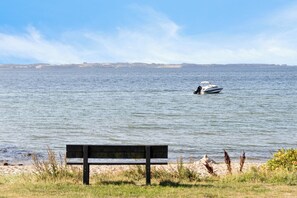 A bench by a calm body of water with a boat in the distance. - Holiday idyll with water views (Rønde)