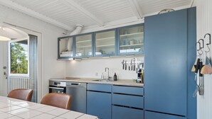 Una cocina moderna con armarios azules, horno empotrado y comedor con mesa y sillas.