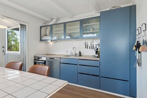 A modern kitchen with blue cabinets, a built-in oven, and a dining area with a table and chairs. - Holiday idyll with water views (Rønde)