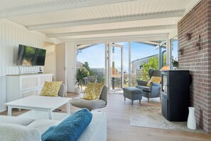 A modern living room with a flat-screen TV, a sofa set, a dining table, and a fireplace. - Holiday idyll with water views (Rønde)