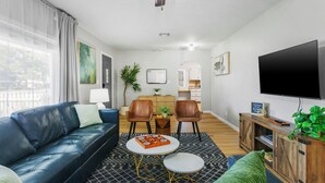 Un salon moderne avec un canapé en cuir bleu, une table basse et un téléviseur. On y trouve deux fauteuils, une petite table avec une plante et un meuble sur lequel est posé un téléviseur.