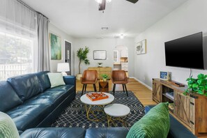 A modern living room with a blue leather sofa, a coffee table, and a TV. There are two chairs, a small table with a plant, and a cabinet with a TV. - Games, Fenced Yard & Covered Trailer Parking (Phoenix)