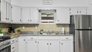 Une cuisine avec des meubles blancs, un réfrigérateur en acier inoxydable, une cuisinière et une fenêtre au-dessus de l’évier.