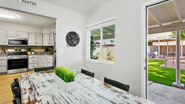 Une cuisine avec des meubles blancs, une horloge et une table à manger avec des chaises.