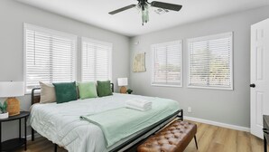 Une chambre à coucher comprenant un lit, un banc, un ventilateur de plafond et une lampe fixée au mur.