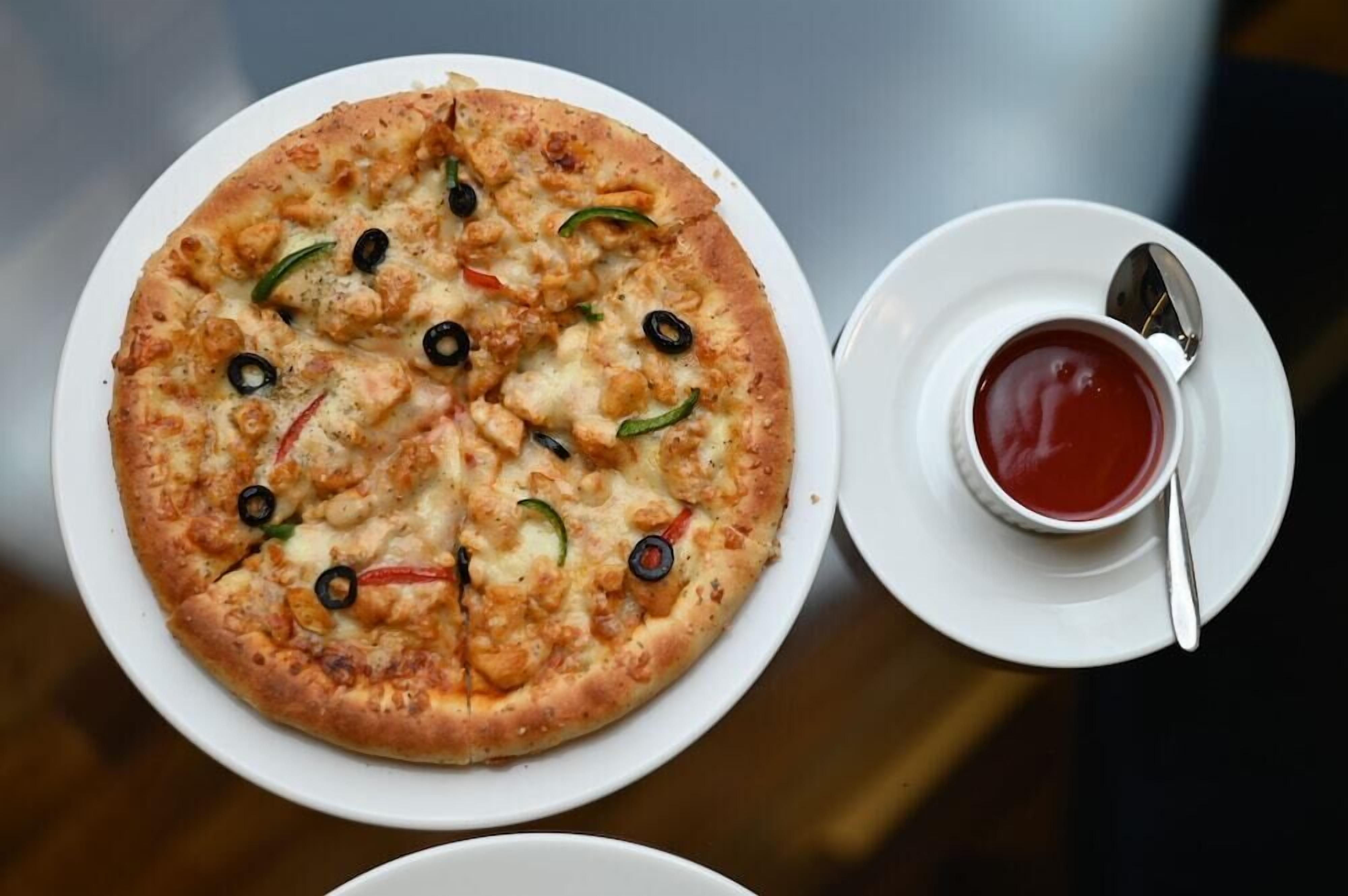A pizza with toppings and a cup of red sauce on a white plate.
