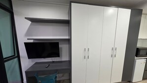 Ett litet rum med ett skrivbord, en tv, en garderob och ett litet kylskåp.