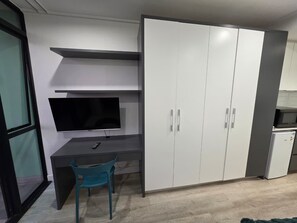 A compact room with a desk, a television, a wardrobe, and a small refrigerator. - Fantastic 1-bedroom studio in vibrant Cape Town near top spots (Cape Town)