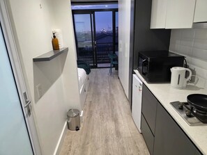 A compact kitchen with a microwave, kettle, and a small sink. A balcony with a city view is visible through the glass door. - Fantastic 1-bedroom studio in vibrant Cape Town near top spots (Cape Town)