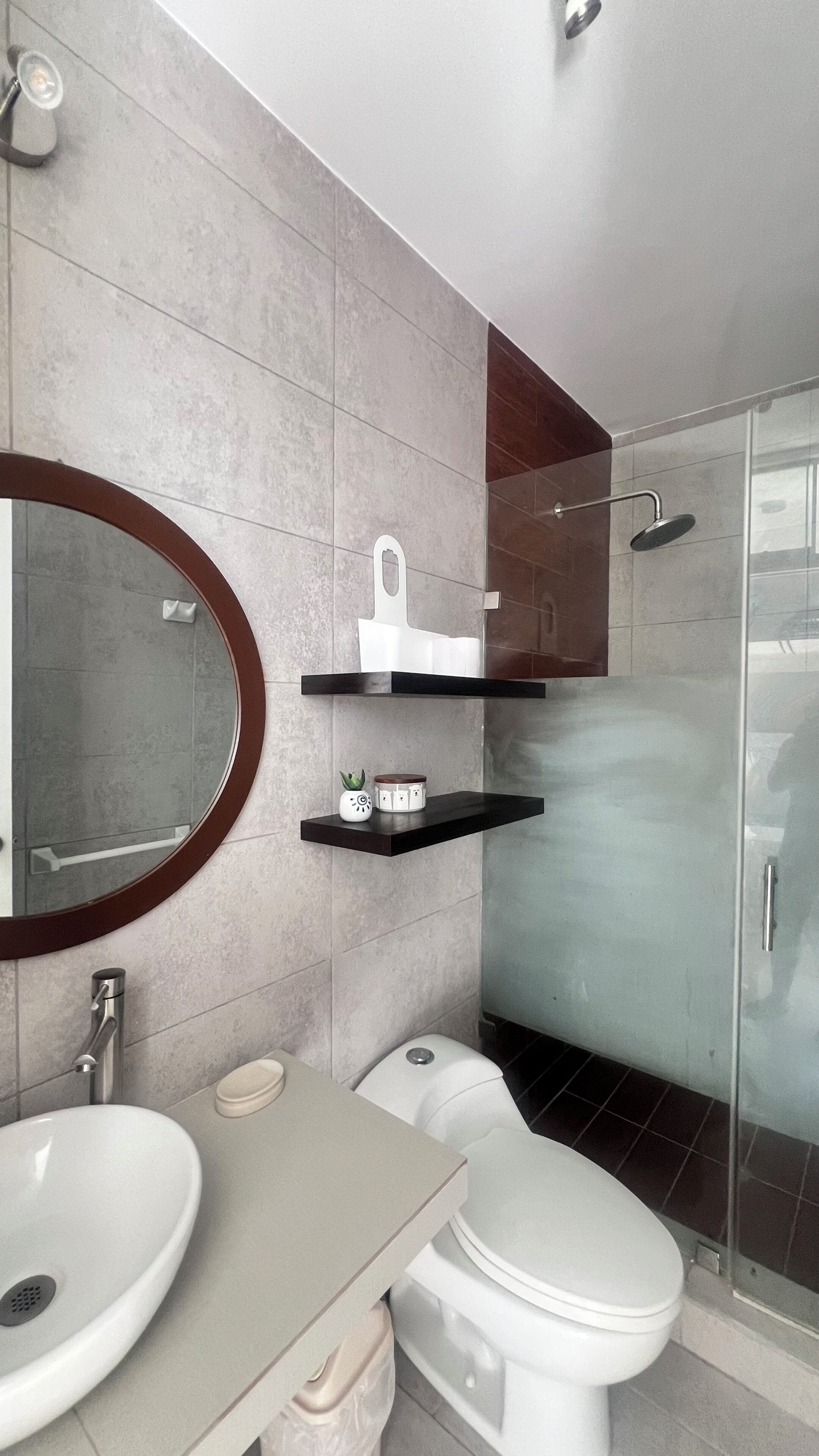 A modern bathroom with a round mirror, a toilet, a sink, and a shower area.