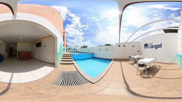 A hotel pool area with a clear sky, a pool, and a lounge area with tables and chairs.