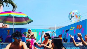 A swimming pool with a mural of sea creatures on the wall, a colorful umbrella, and people enjoying the water.