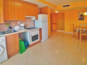 A kitchen with wooden cabinets, a white refrigerator, a toaster, a coffee maker, and a washing machine. - Coral I by Interhome (Miami Platja)