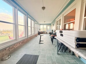 Ein überdachter Patio-Bereich mit einer Reihe von Stühlen und Tischen, große Fenster mit Blick ins Freie und ein Boden aus Steinplatten.